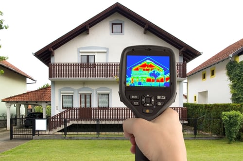 A thermal imaging camera being held outside of a house.